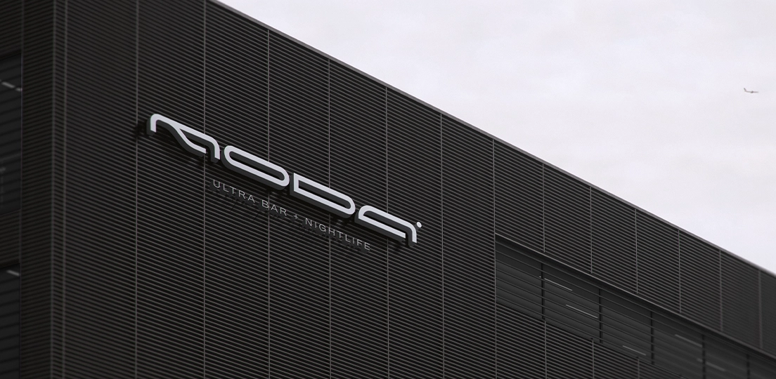 Modern industrial building facade with horizontal black slats and a sign reading 'MODA ULTRA BAR + NIGHTLIFE' against an overcast sky.