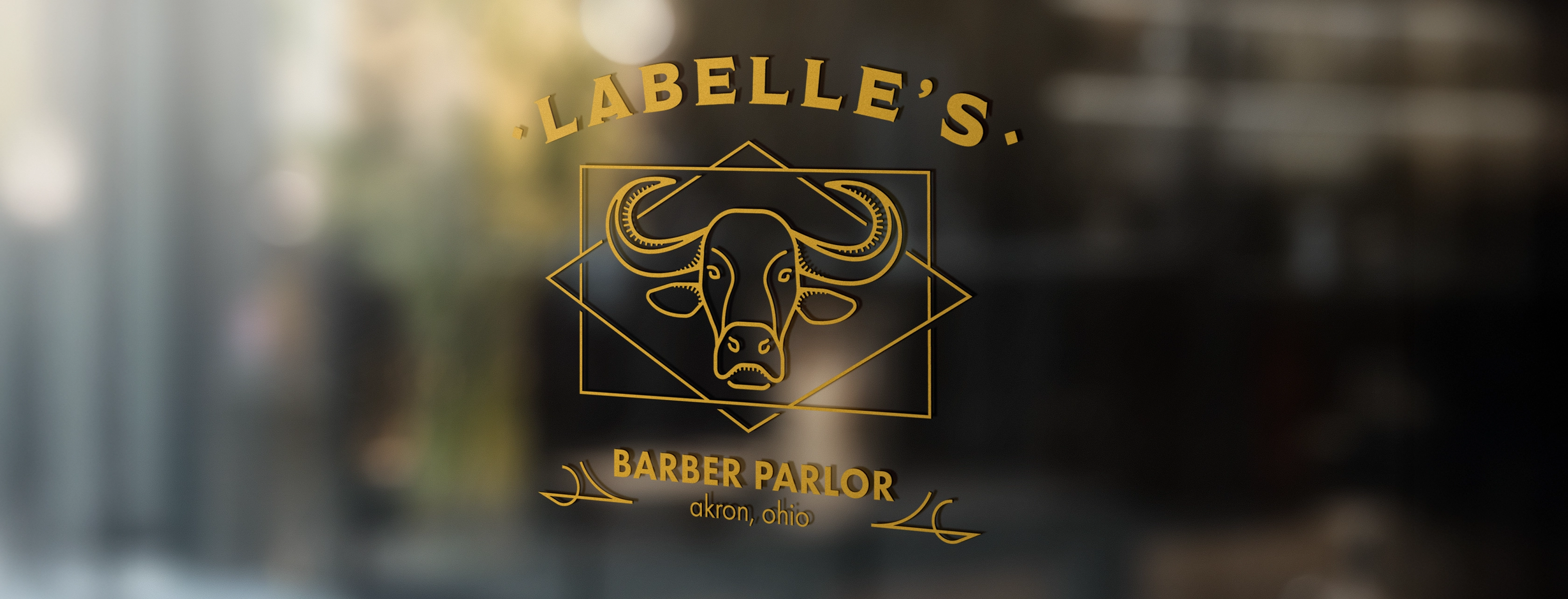Gold lettering on glass showing 'LABELLE'S BARBER PARLOR akron, ohio' with a stylized buffalo head logo.