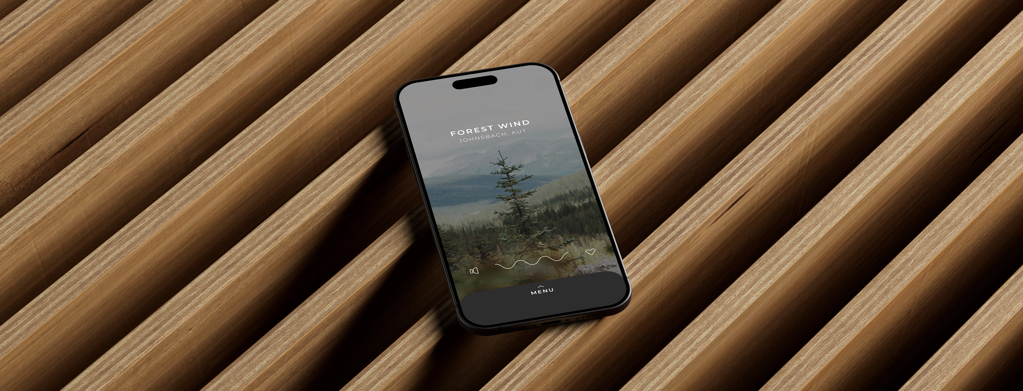 Smartphone displaying an app screen titled 'Forest Wind Johnsbach, AUT' with a pine tree and green mountain background, lying on a modern wooden slatted surface.