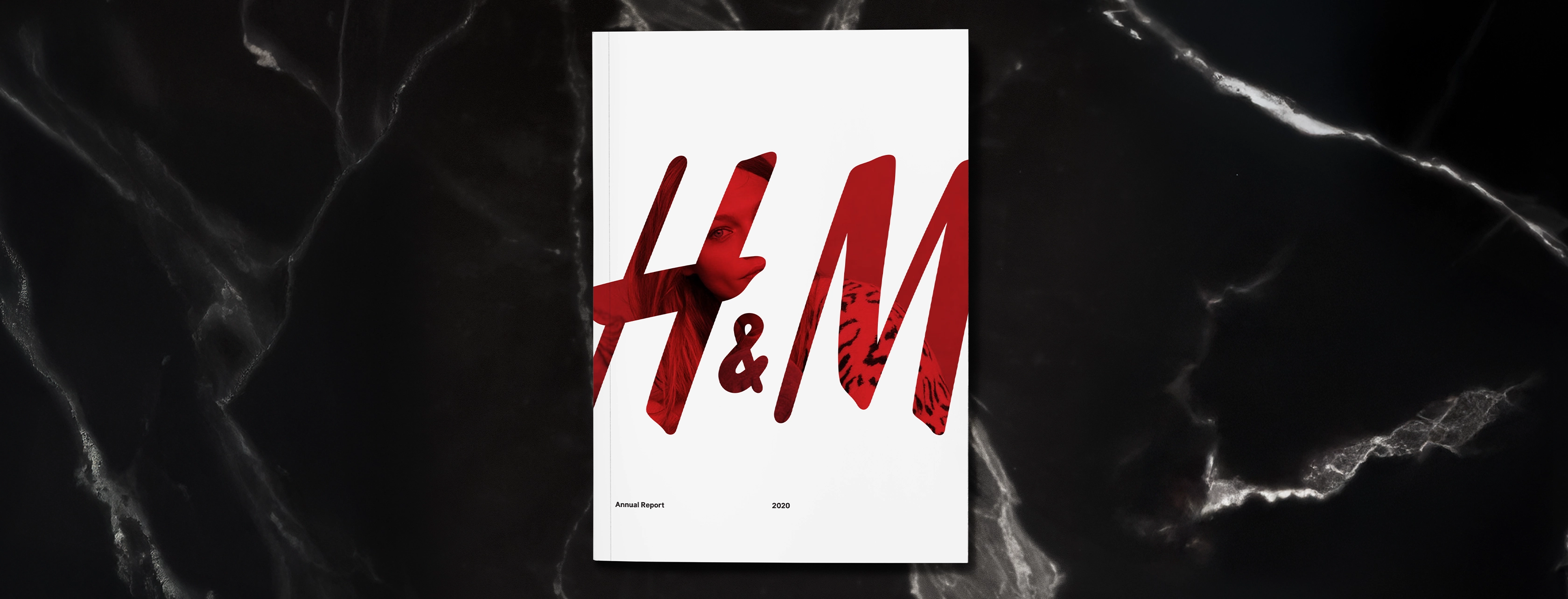 On black granite, a white booklet cover of H&M 2020 annual report with large red H&M logo partially showing a woman in the red of the logo wearing a leopard print shirt.