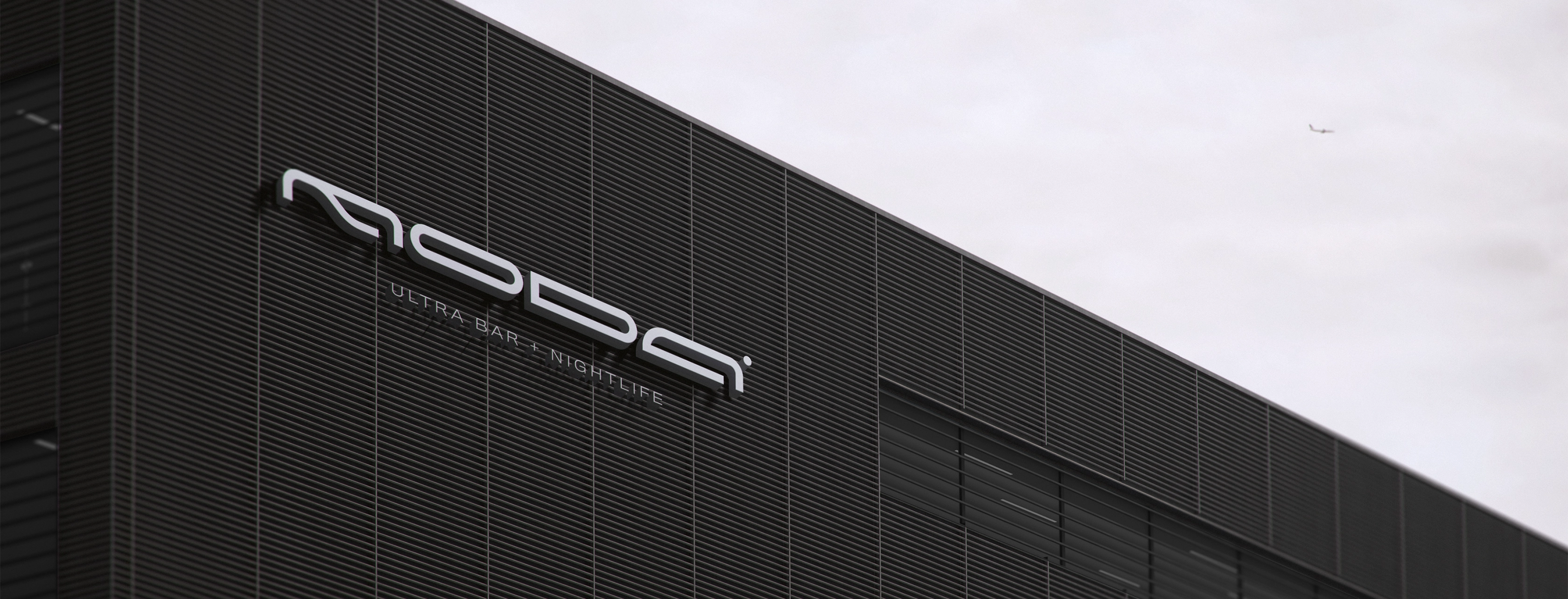 Modern industrial building facade with horizontal black slats and a sign reading 'MODA ULTRA BAR + NIGHTLIFE' against an overcast sky.