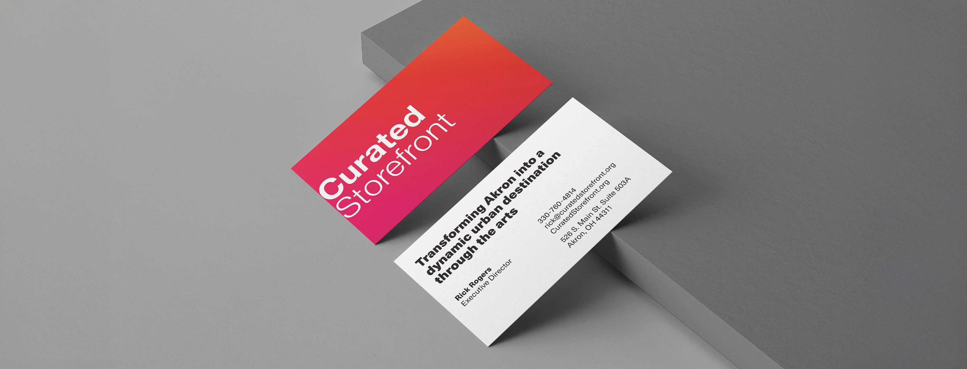 Two business cards, one with 'Curated Storefront' in white text on a red-orange gradient background, the other with contact info for Rick Rogers, Executive Director of Curated Storefront, including phone, email, website, and address in Akron, Ohio.