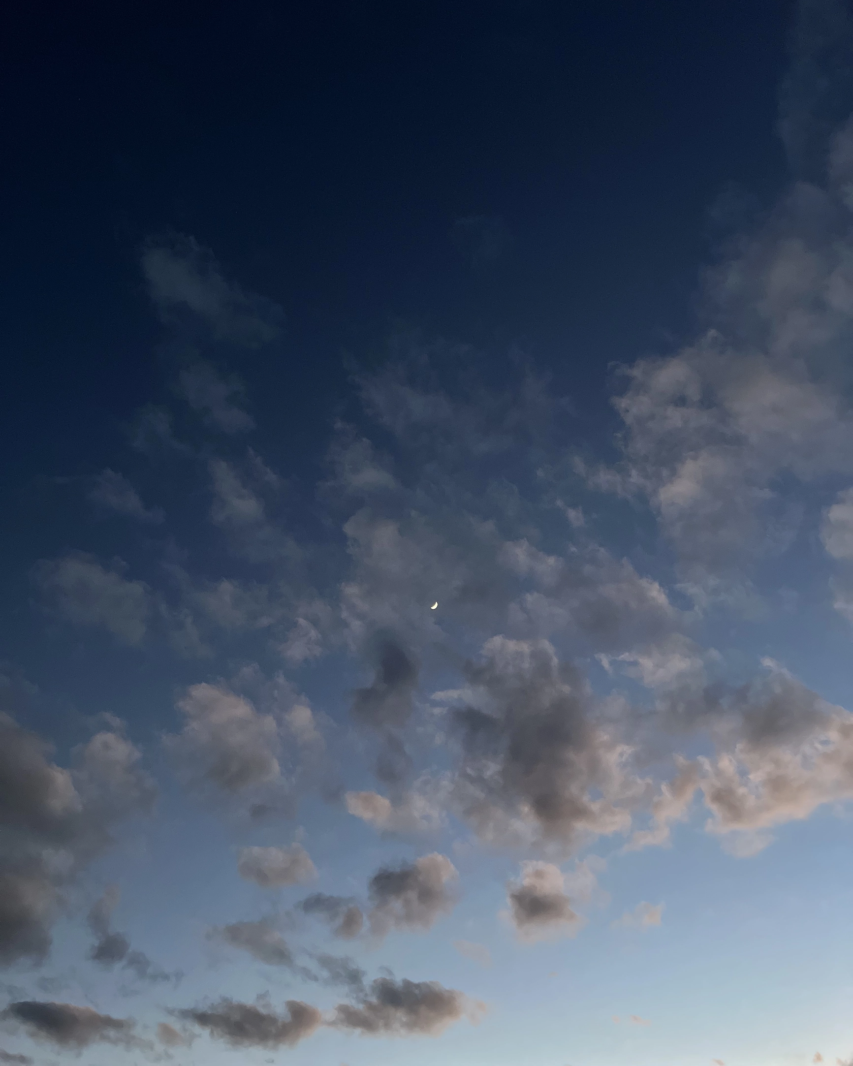 Evening sky with scattered clouds and a thin crescent moon.