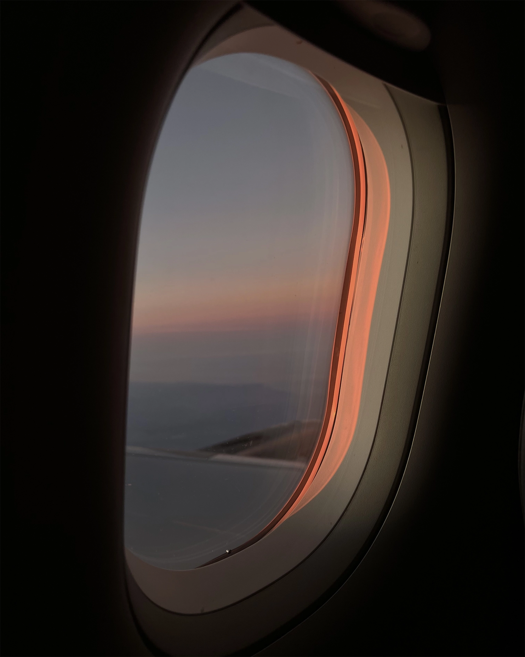 View through an airplane window showing a wing and a colorful sunset sky with orange and pink hues.