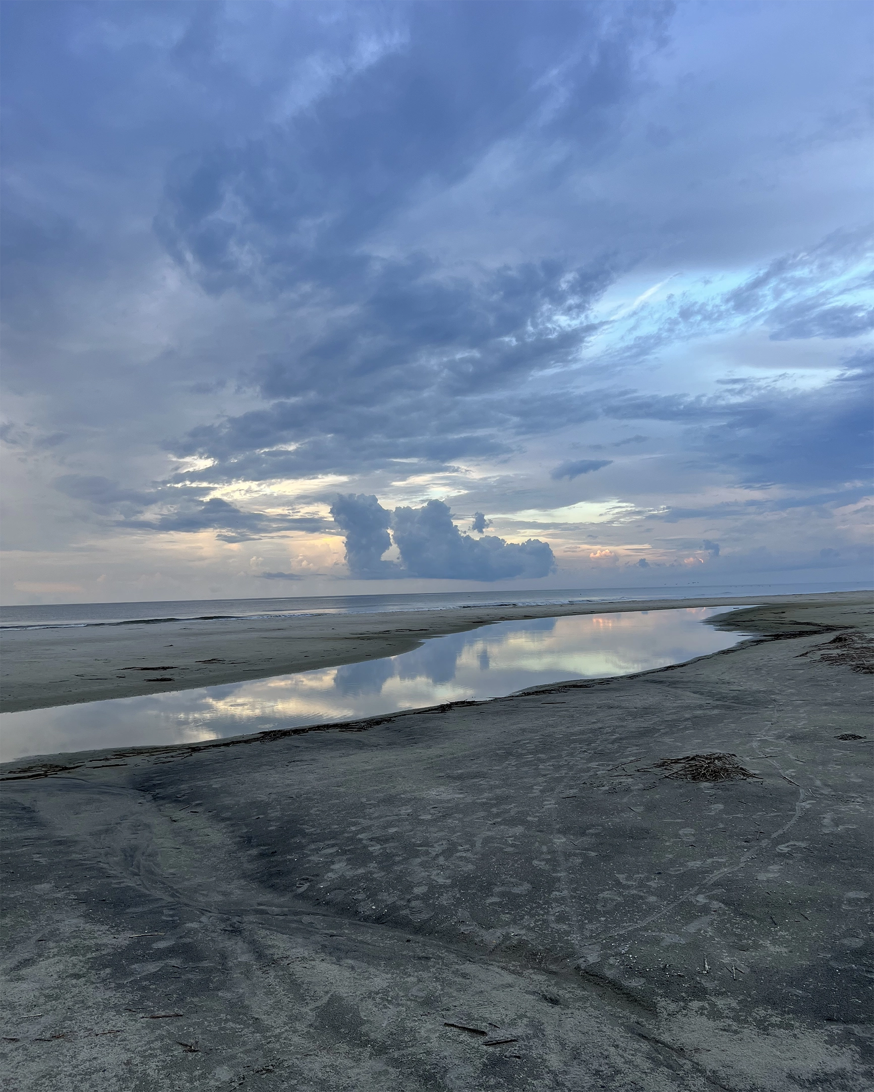 Calm beach scene at sunset with tidal pool reflecting clouds and blue sky.