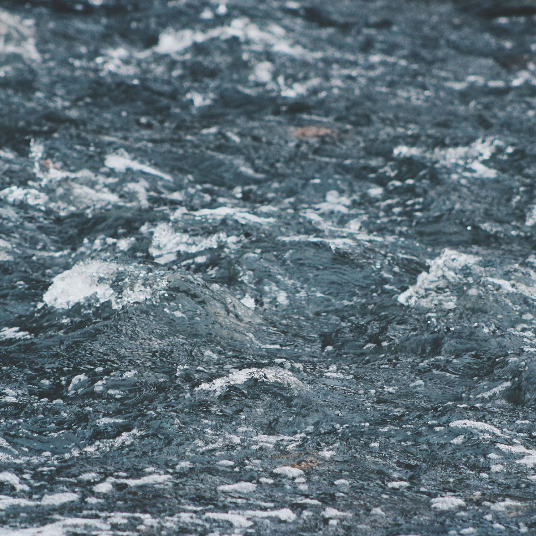 Close-up of dark, rippling water with small waves and foam.