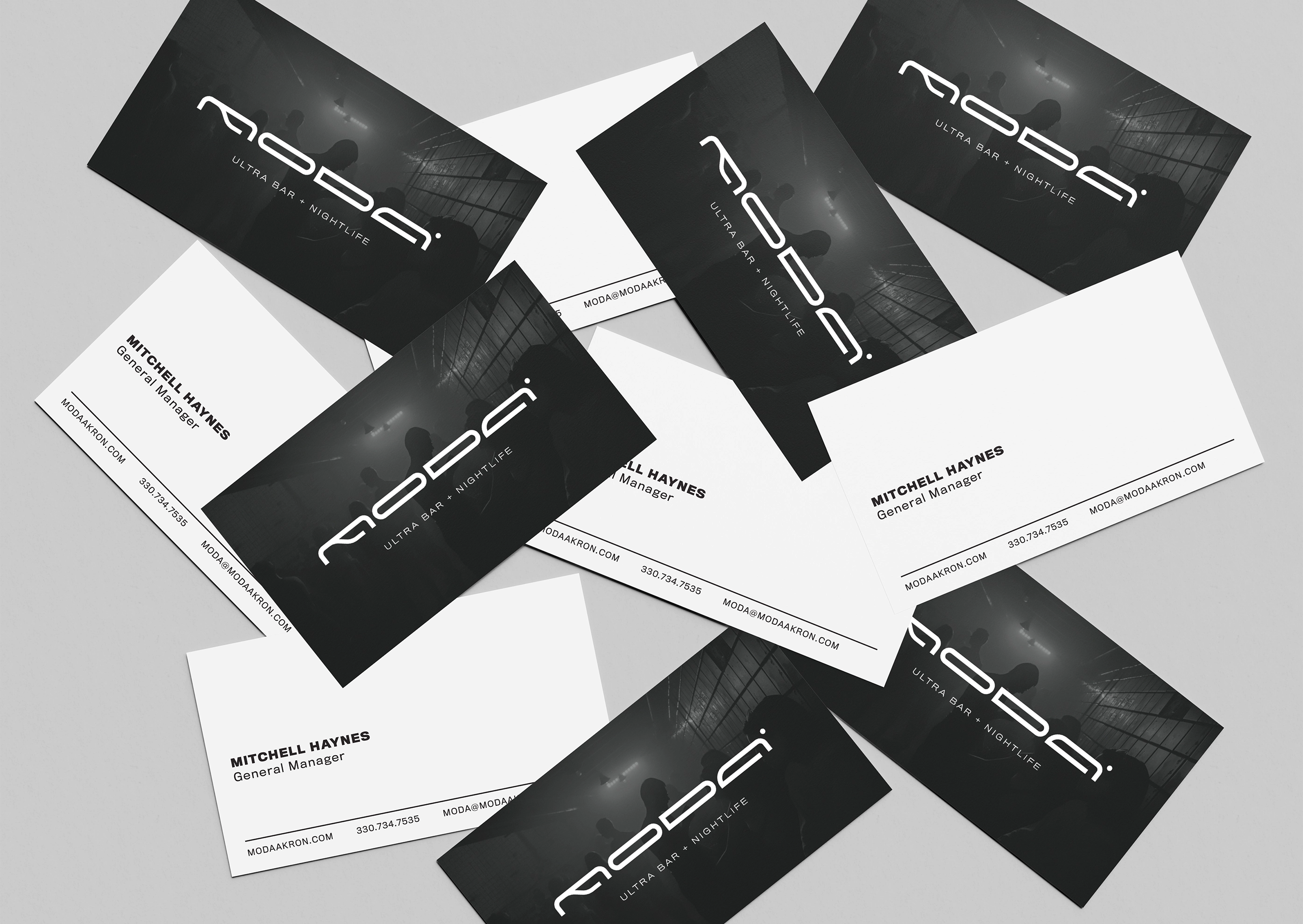 Scattered business cards with the MODA Ultra Bar and Nightlife logo depicted on one side in white on a dark background. The other side of the card is white with a generic "General Manager" contact listed.