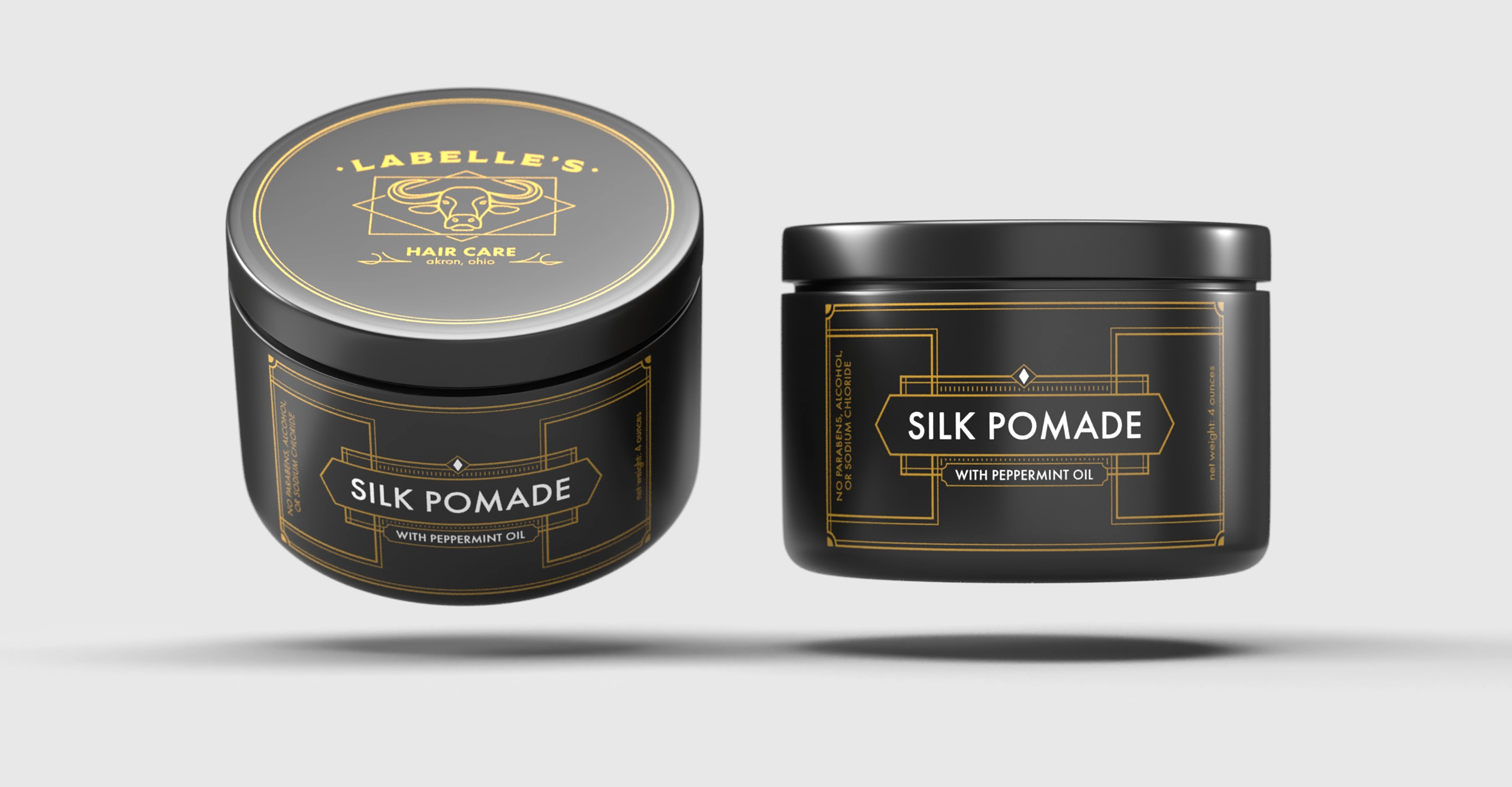 Two black floating cylindrical containers of Labelle’s Silk Pomade with peppermint oil, featuring gold geometric designs and branding.