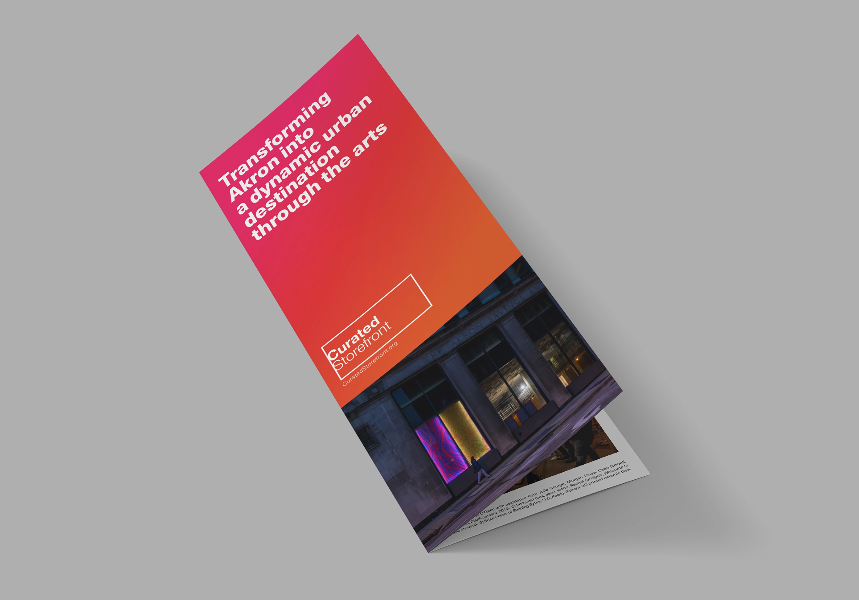 Trifold brochure with a red gradient cover reading 'Transforming Akron into a dynamic urban destination through the arts' above an image of illuminated storefront windows at night.