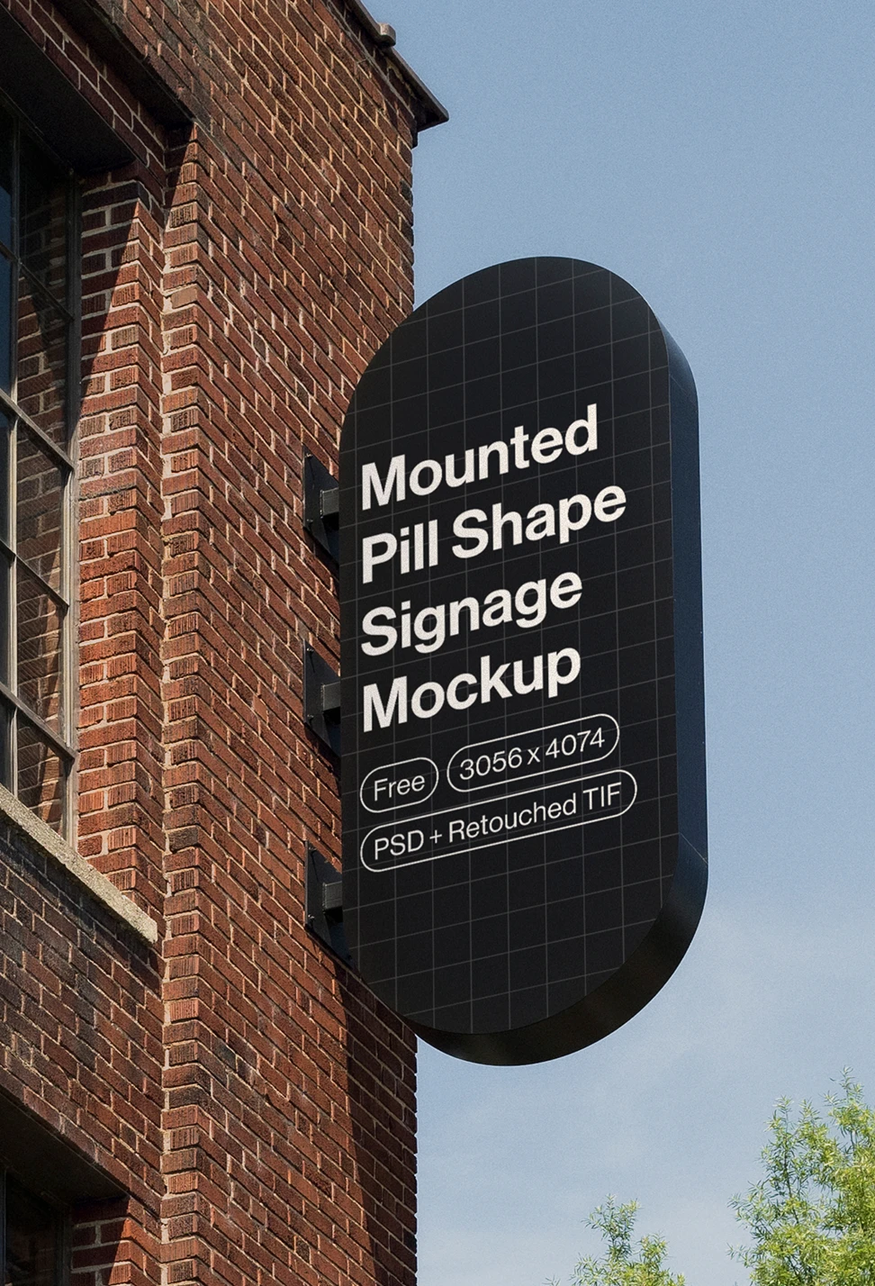 Black pill-shaped signage mounted on a brick building under a clear blue sky with green trees nearby.
