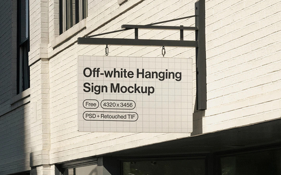 Off-white hanging sign with text mounted on a light brick building facade next to green tree branches.