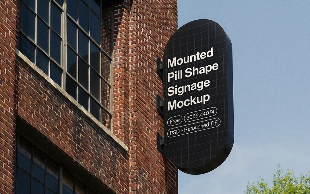 Black pill-shaped signage mounted on a brick building under a clear blue sky with green trees nearby.