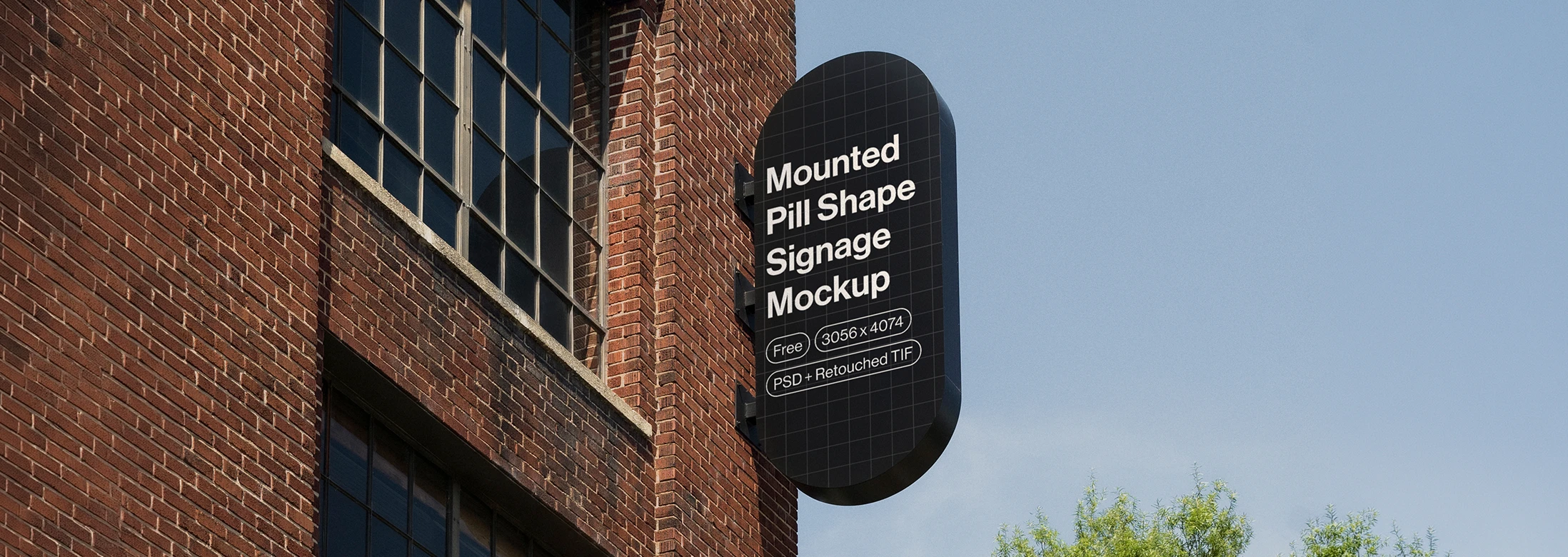 Black pill-shaped signage mounted on a brick building under a clear blue sky with green trees nearby.