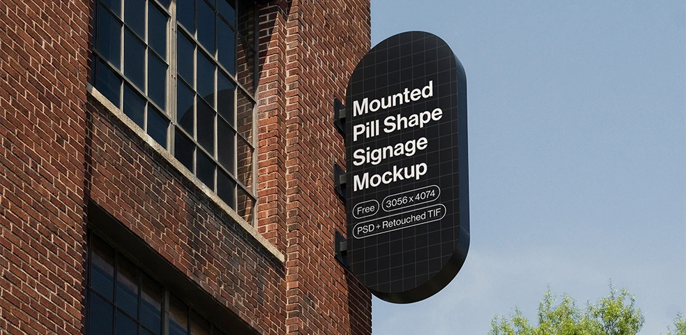 Black pill-shaped signage mounted on a brick building under a clear blue sky with green trees nearby.