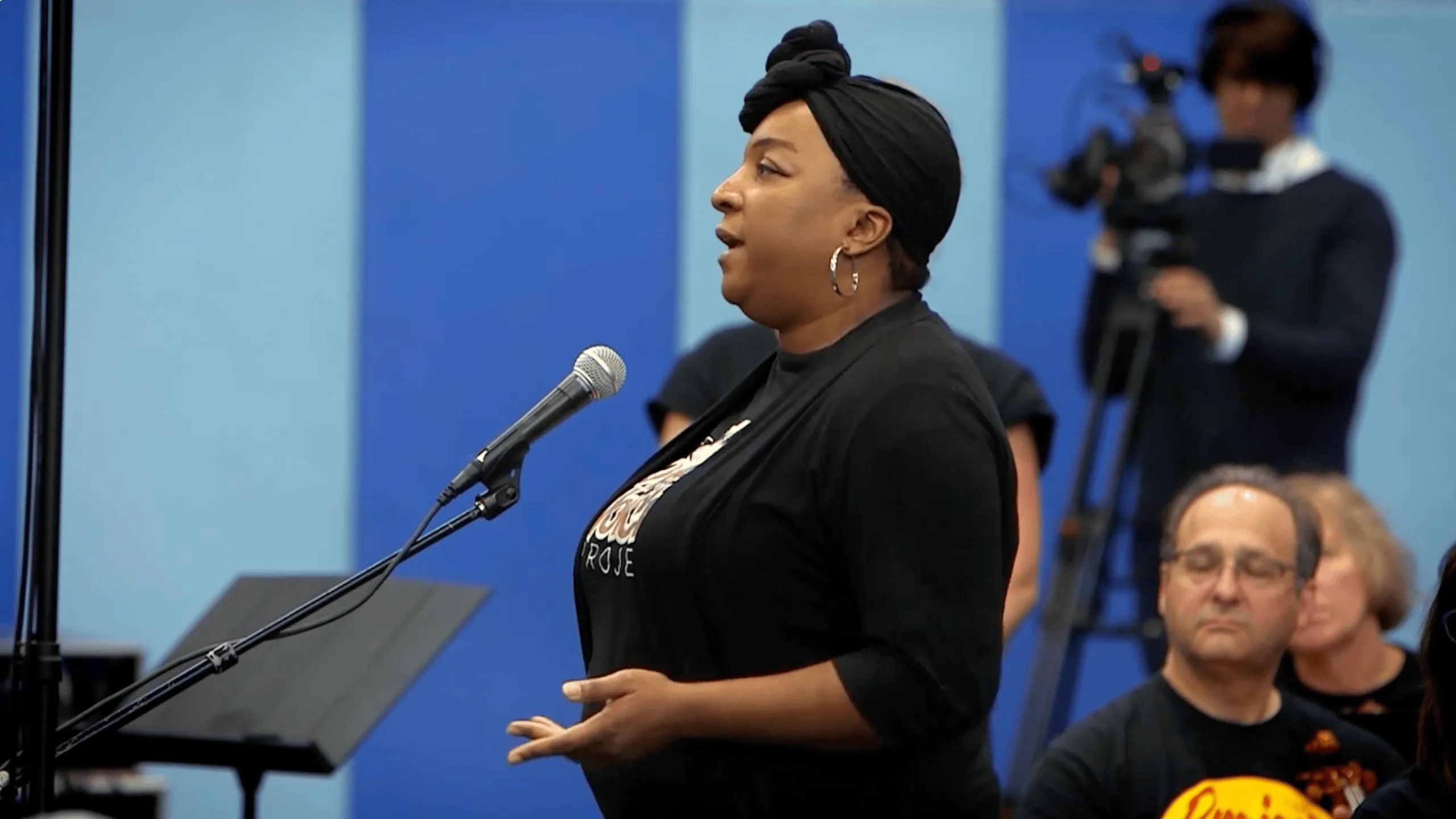 Woman singing into a microphone during a performance on a blue-lit stage
