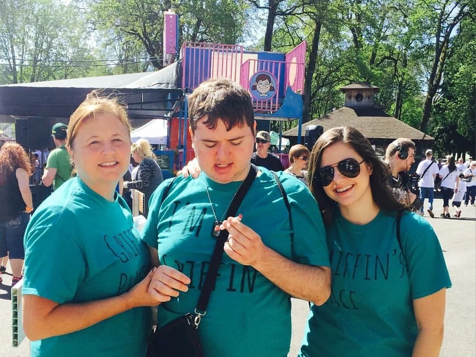 Three people in matching Griffin's Place shirts smiling together at a sunny outdoor community festival