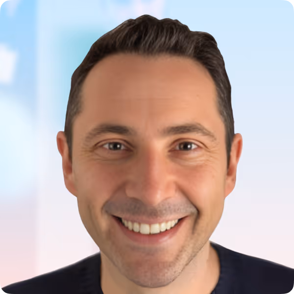 Smiling man with short dark hair against a light blue and soft pink gradient background.
