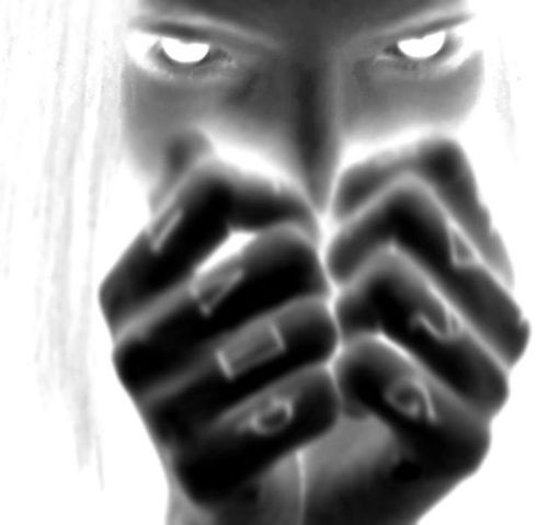 Negative-style close-up of a person with intense eyes holding their clenched fists near their face.