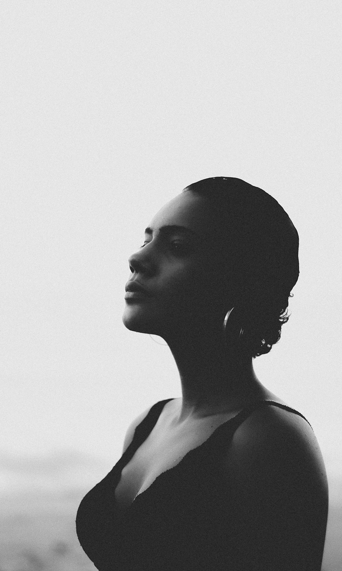 Black and white profile portrait of a woman wearing hoop earrings and a sleeveless top against a bright background.