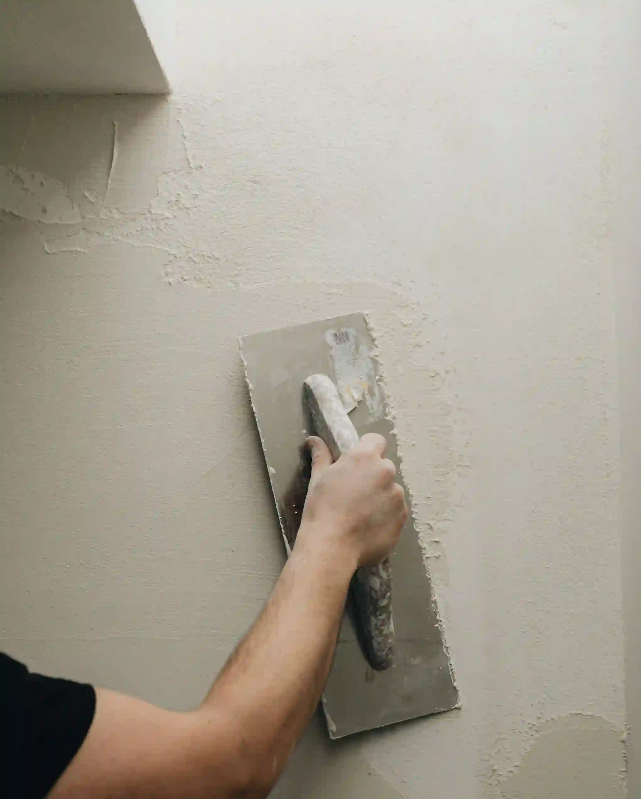 Professionele stucadoor brengt glad lichtgekleurd stucwerk aan op muur met rechthoekige truweel