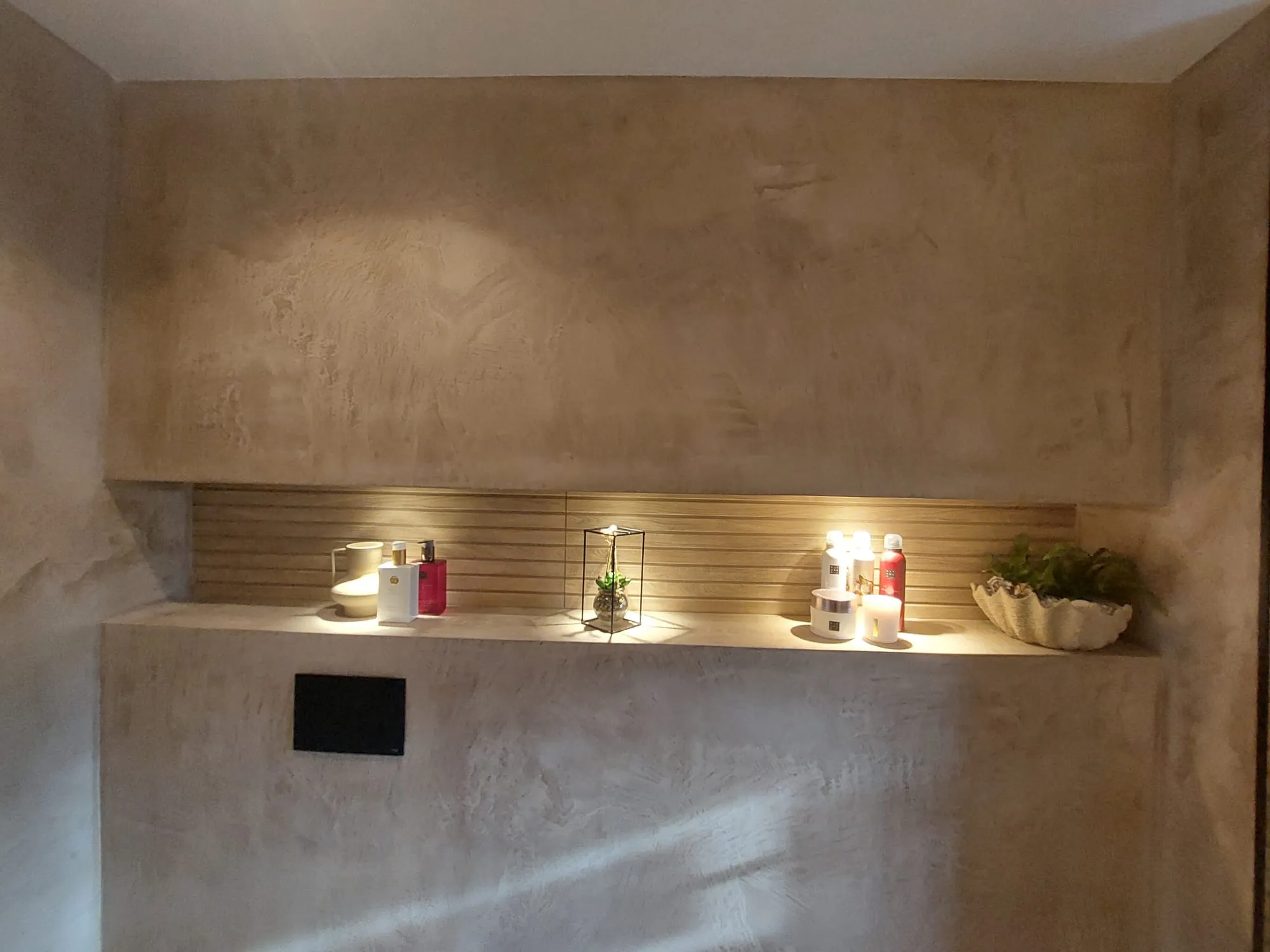 Beige gestructureerd decoratief stucwerk met ingebouwde plank voor decoratieve items, kandelaars en planten
