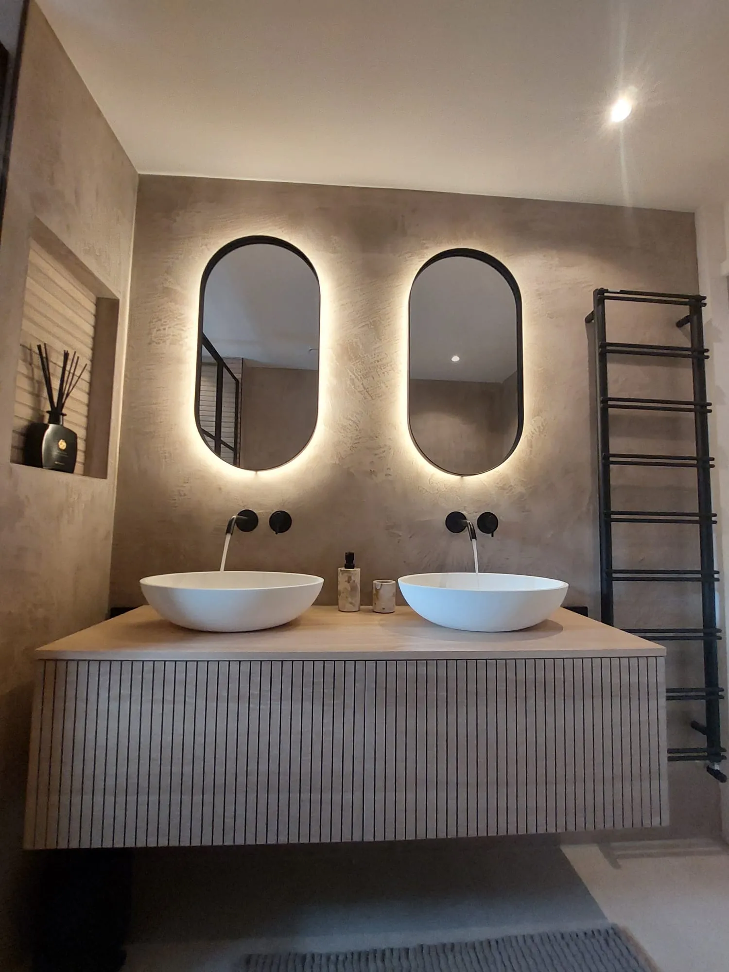 Modern badkamermeubel met glad stucwerk afwerking, ovale opzetwastafels, verlichte spiegels en wandkranen
