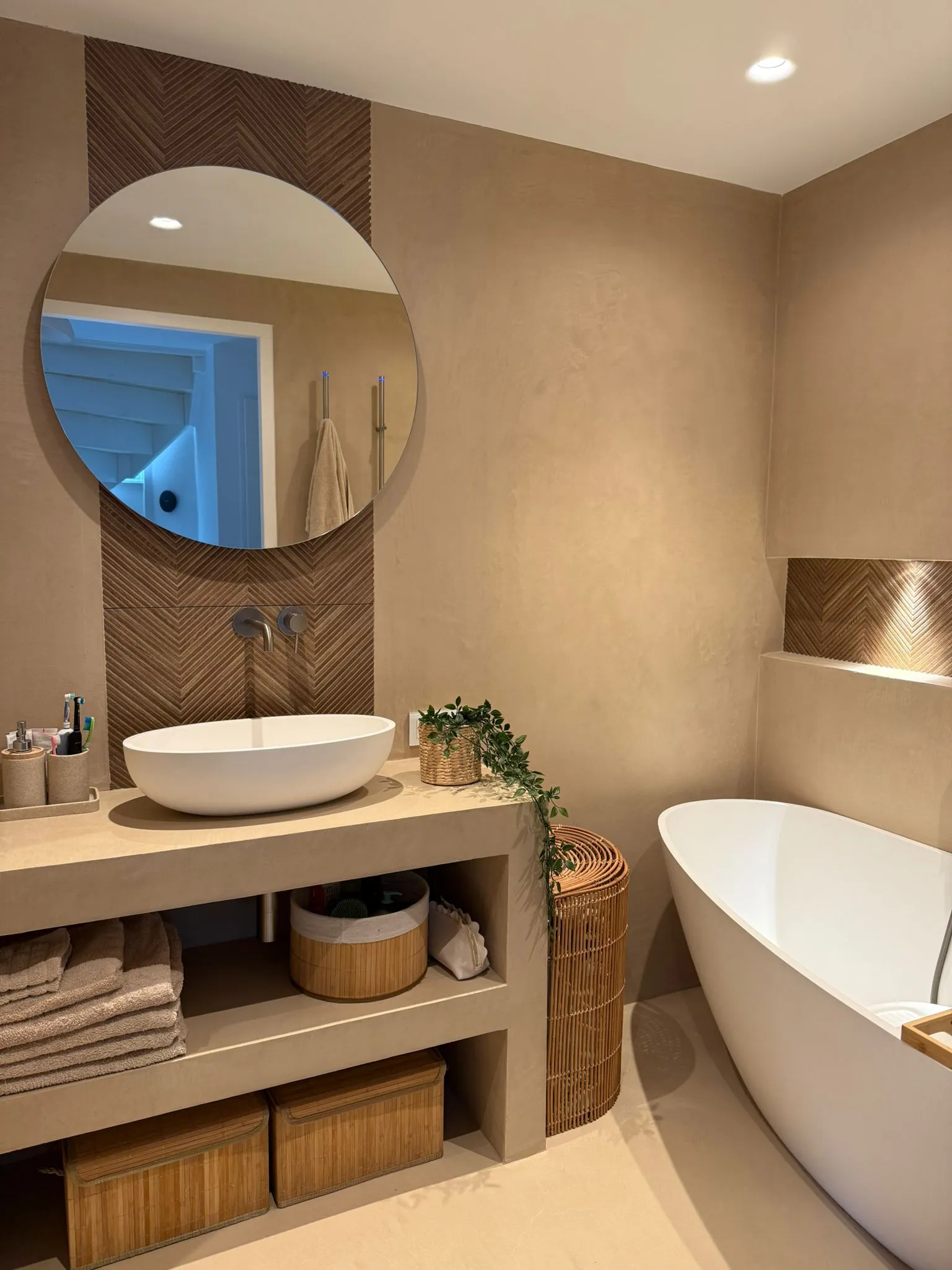 Moderne badkamer met glad stucwerk afwerking, beige blad met opzetwastafel, ronde spiegel en vrijstaand bad
