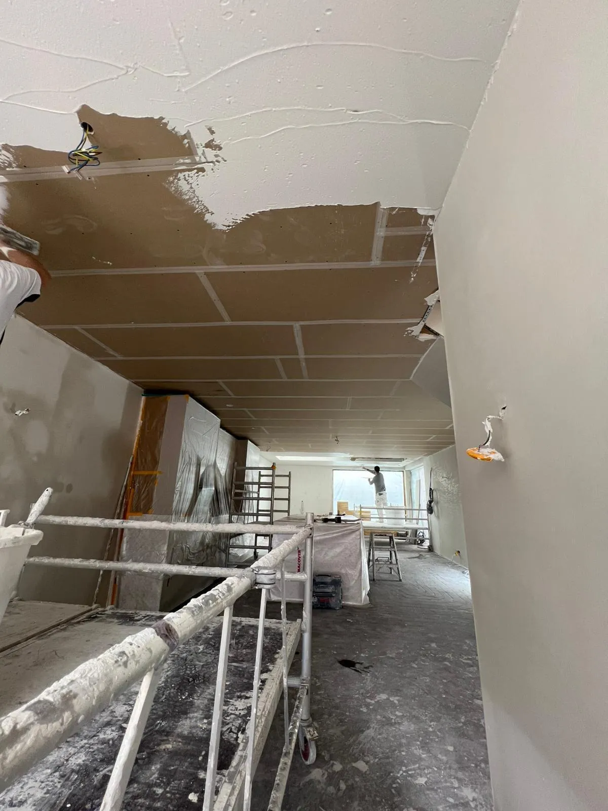 Twee stucadoors werken vanaf steiger aan plafond stucwerk tijdens renovatie met afgedekte meubels
