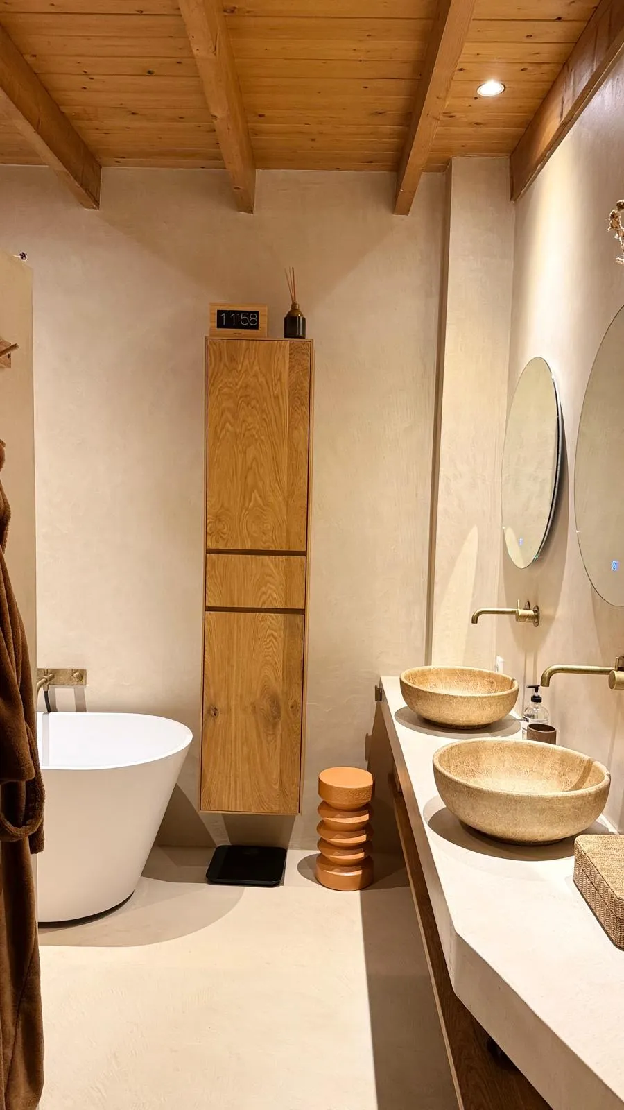 Luxe badkamer met glad stucwerk, houten plafondbalken, vrijstaand bad en natuurstenen wastafels
