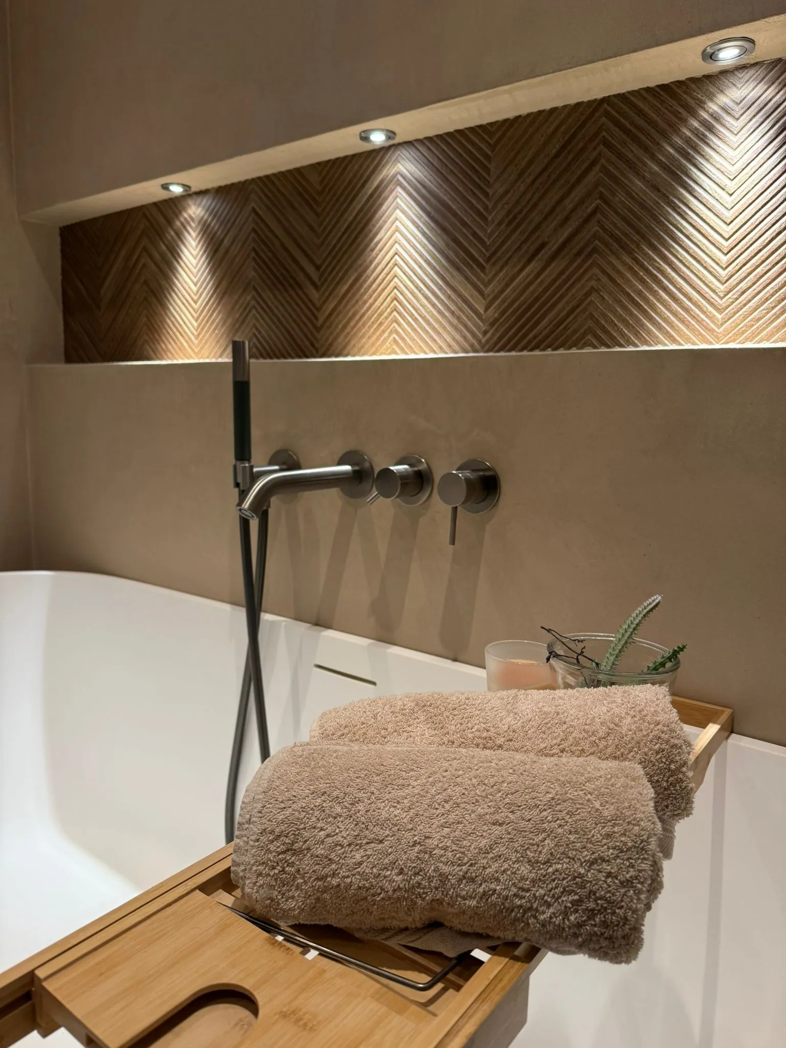 Moderne badkamer met beige stucwerk wandafwerking, vrijstaand bad en wandgemonteerde kranen onder accentverlichting