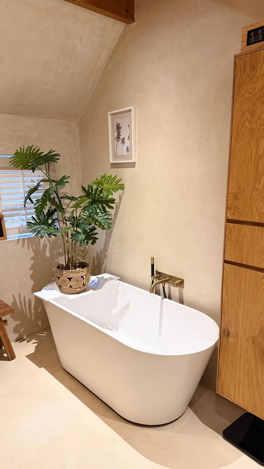 Minimalistische badkamer met beige sierpleister gestructureerd stucwerk, vrijstaand bad en houten kastje