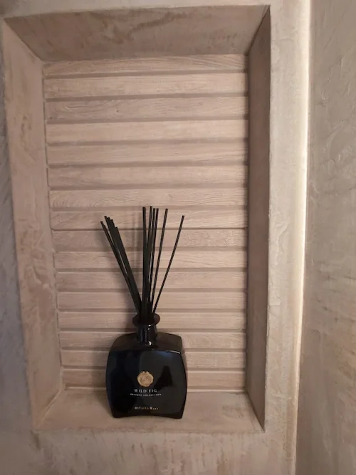 Ingebouwde wandnis in beige stucwerk met houten lattenachtergrond en decoratieve geurstokjes
