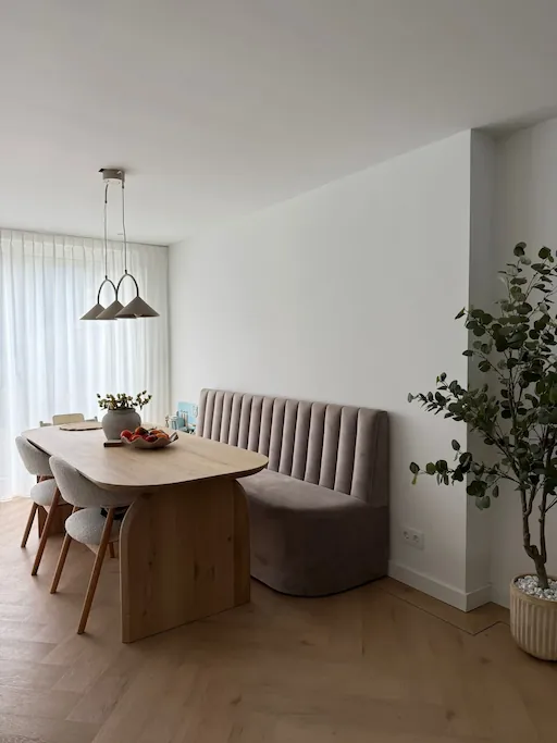 Minimalistische eetkamer met glad wit stucwerk op muren en plafond, houten tafel en hanglampenen
