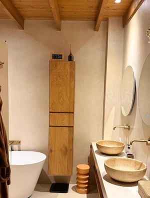 Luxe badkamer met glad stucwerk, houten plafondbalken, vrijstaand bad en natuurstenen wastafels
