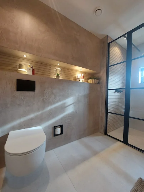 Modern toilet met beige decoratief gestructureerd stucwerk, wandgemonteerde WC, ingebouwde nis en glazen douchewand
