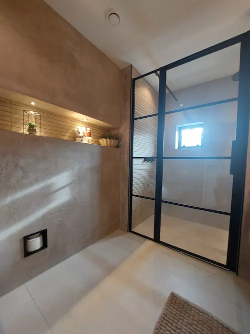 Moderne badkamer met beige gestructureerd sierpleister stucwerk, inbouwnis en zwart glazen douchewand
