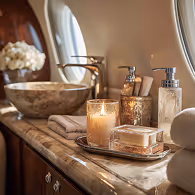 Luxurious private jet bathroom countertop with lit candle, soap dispenser, lotion bottle, towels, and stone sink under oval window.