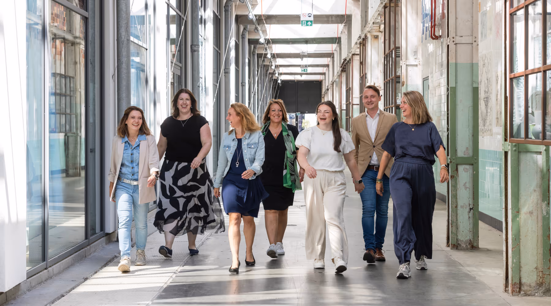 7 lachende, lopende NieuweStroom collega's in het kantoor van NieuweStroom.