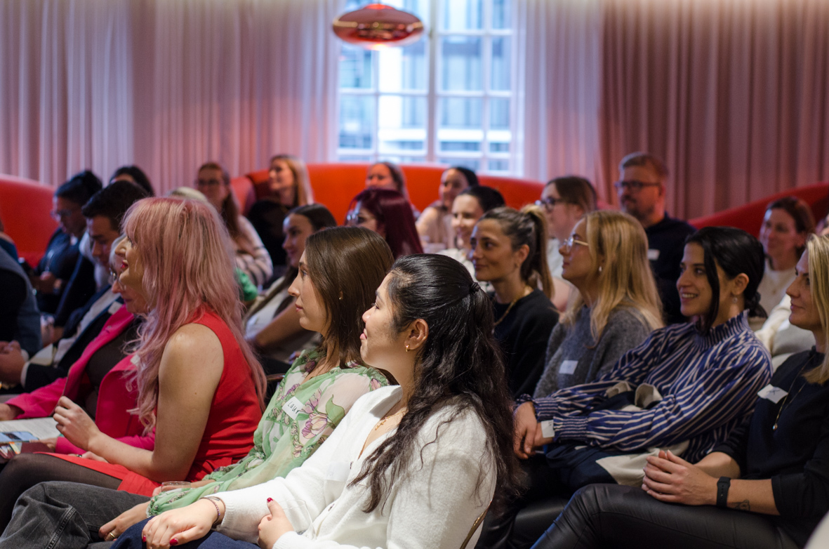 Group of people attentively listening in a conference or seminar room with warm lighting and large windows.