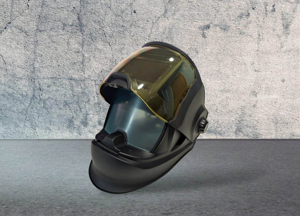 Black welding helmet with a tinted gold face shield and adjustable knob on side, placed on a gray surface with a textured wall background.