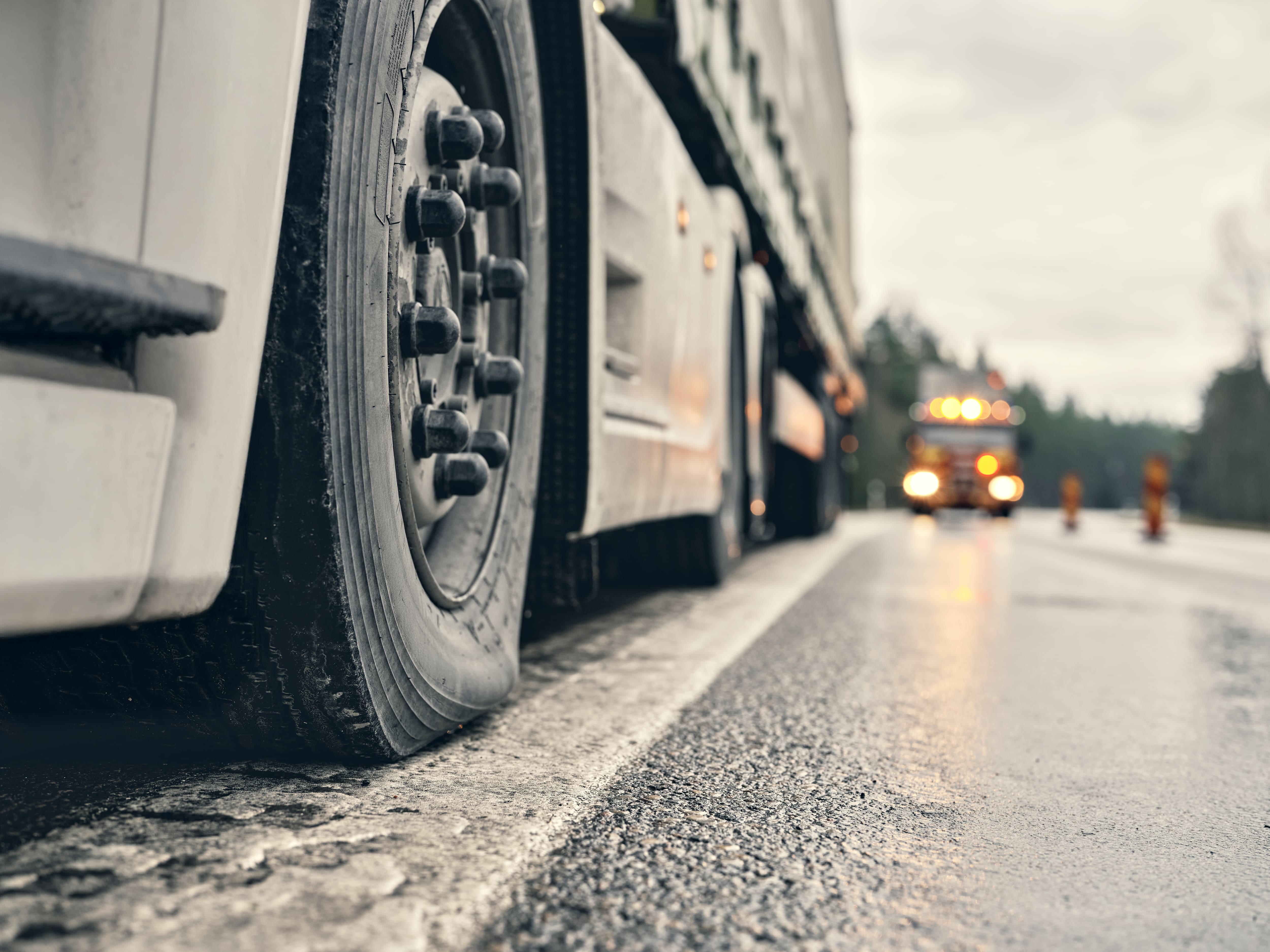 Close-up of a flat tire on a large truck parked on the roadside with another vehicle approaching in the background.