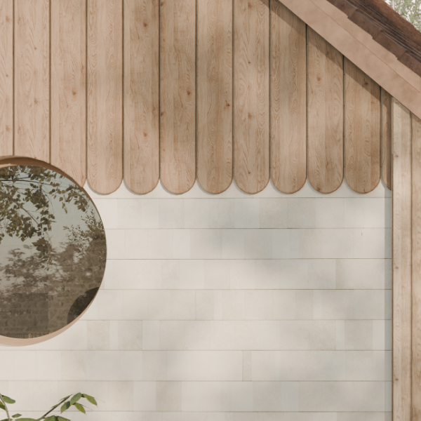 Exterior wall with light wood scalloped siding at the top and white horizontal stone tiles below with a round window reflecting tree branches.