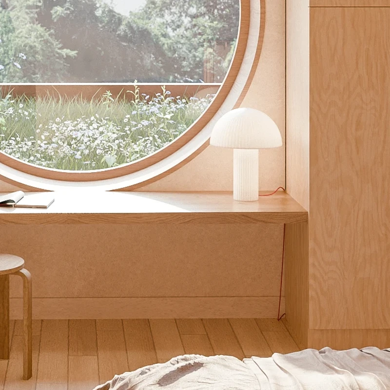 Minimalist bedroom with light wood paneling, a round window with a scenic view, a wooden desk, a stool, and a small modern lamp.