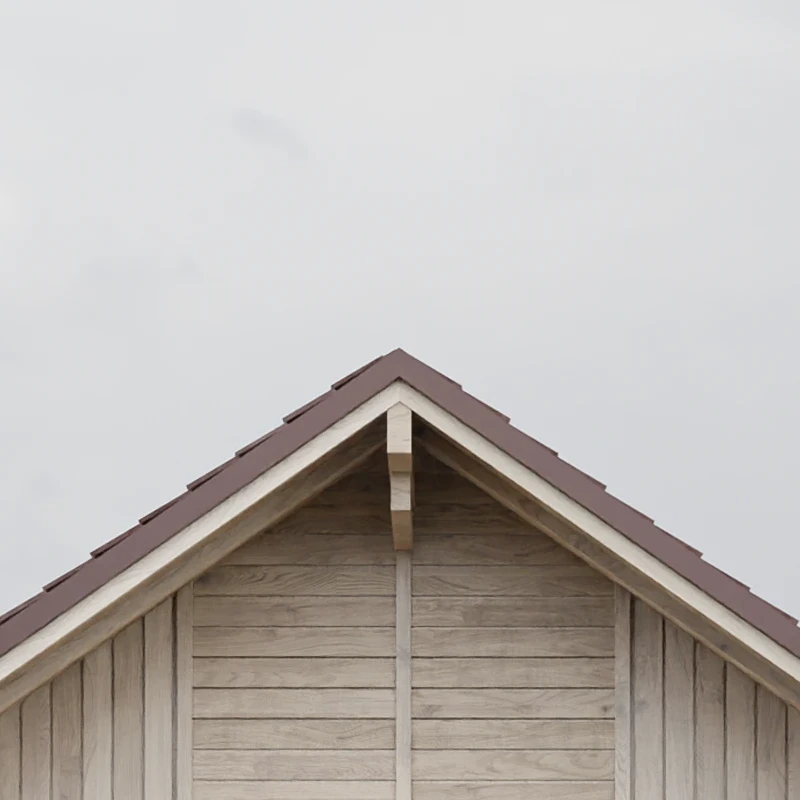 Close-up of a wooden house gable with a brown sloped roof against a cloudy sky.