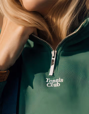 Close-up of a person wearing a green zip-up top with the words 'Tennis Club' embroidered below the zipper.