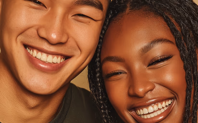 Close-up of a smiling Asian man and Black woman with braided hair, showing their teeth.