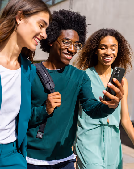 Three smiling young adults walking outdoors and looking at a smartphone together.
