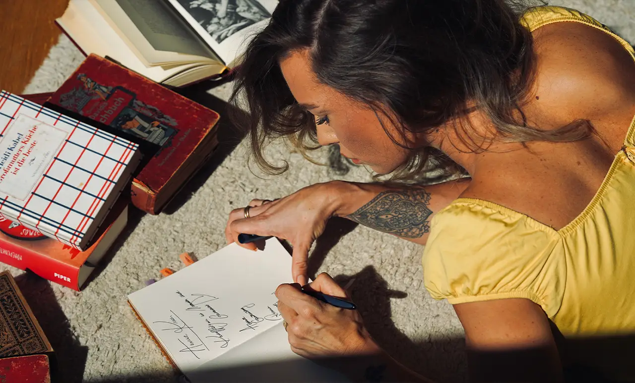 Anna liegt auf dem Boden zwischen offenen Büchern und schreibt in ein Notizheft. Das Motiv steht für Wissen, Reflexion und die Lernreise in der Anatomie Academy.