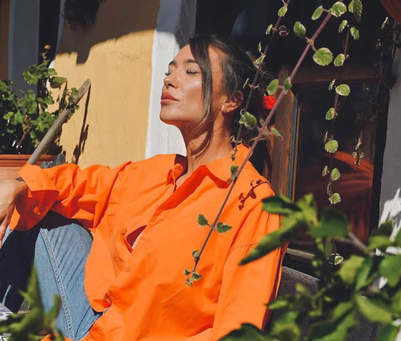 Anna Hahn sitzt in der Sonne, trägt ein orangefarbenes Hemd und genießt einen Moment der Ruhe – Sinnbild für Selbstakzeptanz und Genuss ohne Zwang.