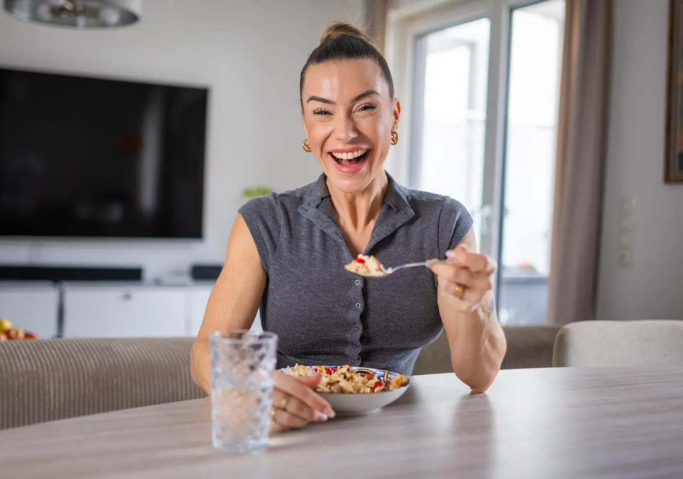 Anna Hahn sitzt lachend am Tisch und isst eine gesunde Mahlzeit – Symbol für Balance, Lebensfreude und Wohlbefinden nach ihrer 50-Kilo-Abnahme.